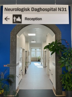 Et billede af en hospitalsgang med et skilt, der henviser til Neurologisk Daghospital N31, receptionen.