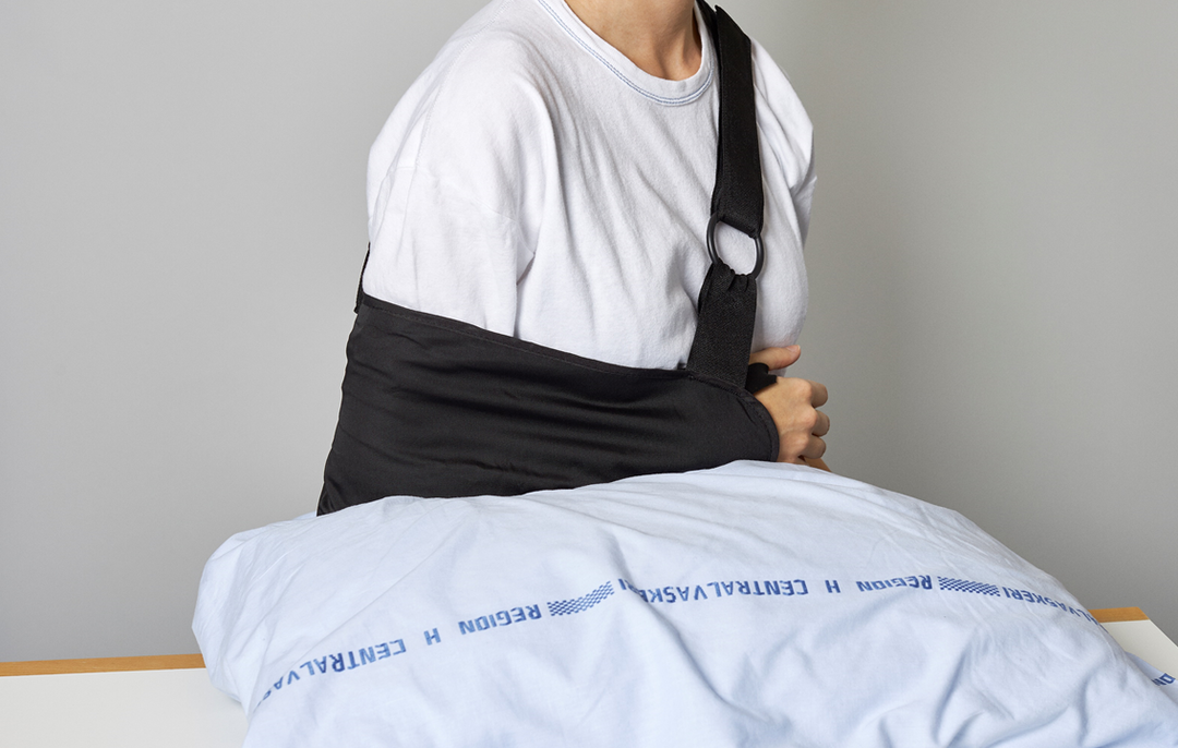 Foto af en patient, der sidder ned og hviler sin underarm på en pude foran sig.