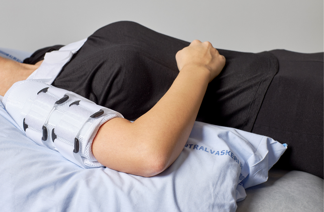Foto af en person, der ligger på ryggen med en pude under overarmen og hånden på maven.