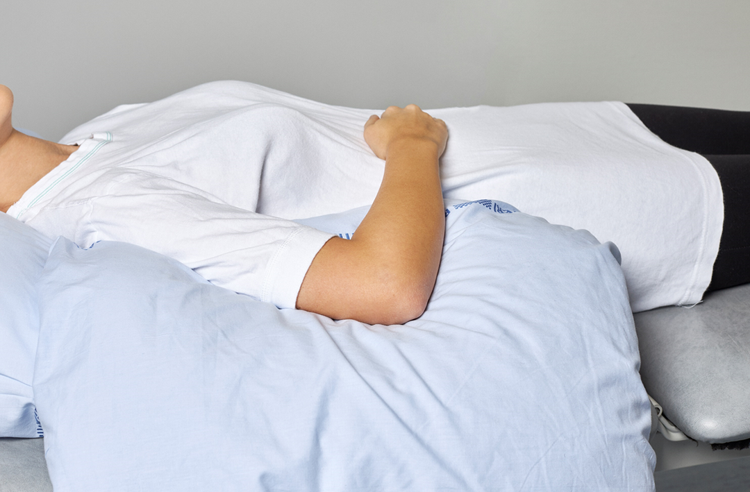 Foto af en patient, der ligger på ryggen med en pude under overarmen og armen på maven.