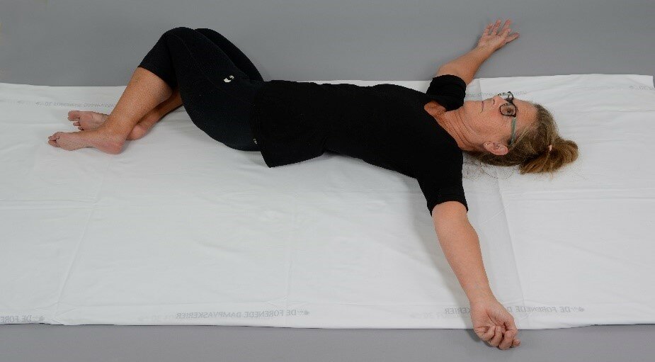 Et billede af en kvinde, der ligger i en seng med armene ud til siden.