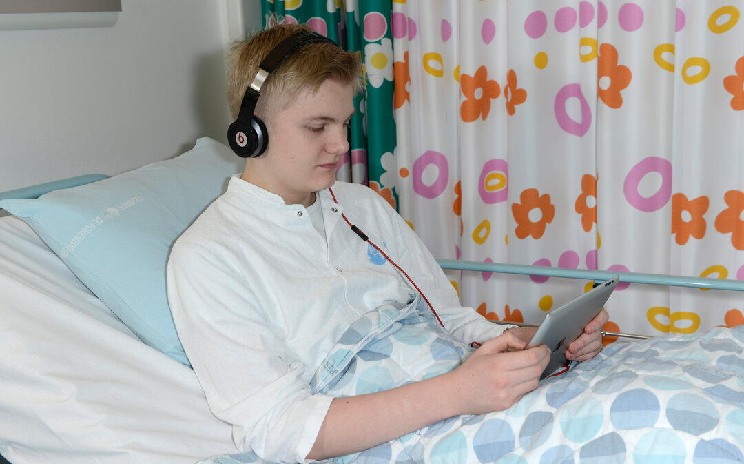 Et foto af en ung dreng, der sidder i en hospitalsseng. 