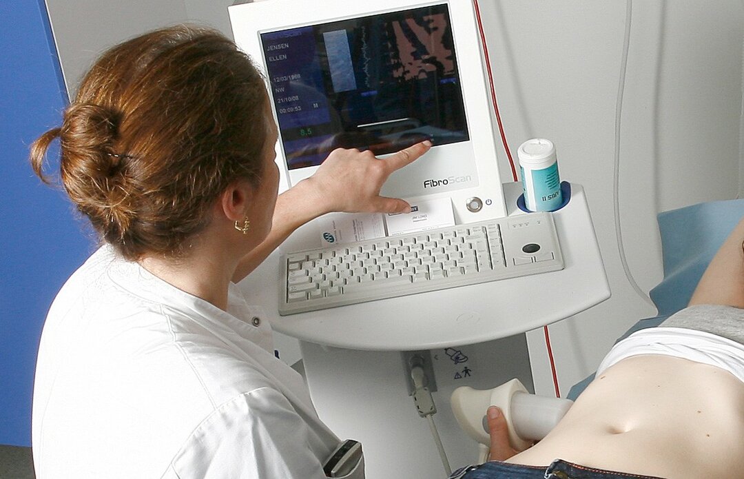 Billedet viser en fibroscanning. Sygeplejersken/lægen placerer et lille apparat på huden over leveren. På skærmen kan man med det samme se tegn på, om der er arvæv i leveren.