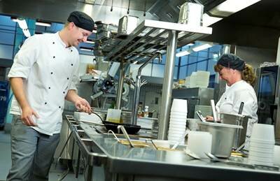 Billedet viser to køkkenansatte der laver mad ved et komfur.