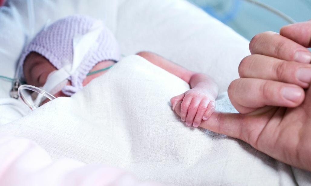 Nyfødt barn med sonde holder om forælders finger