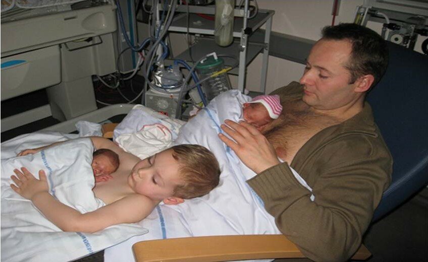 Far og storebror i hud-mod-hud kontakt til nyfødte babyer