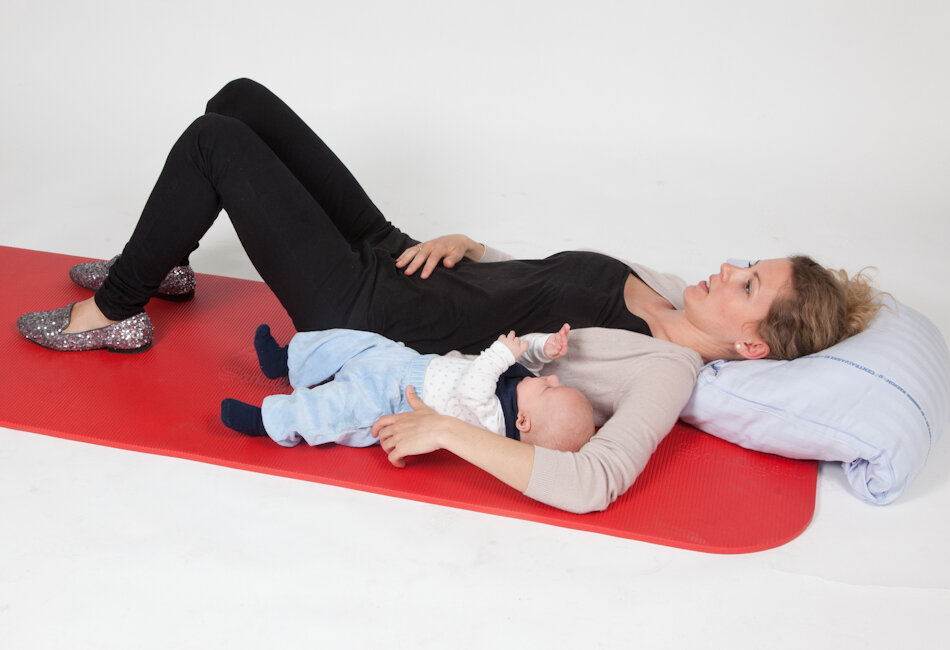 Billedet viser en mor med sit barn på en yogamåtte.