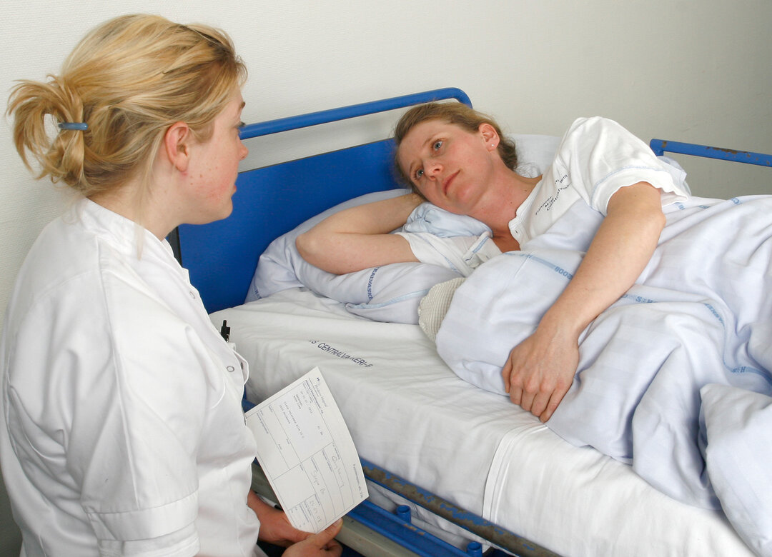 The picture shows a nurse talking to a patient lying down.