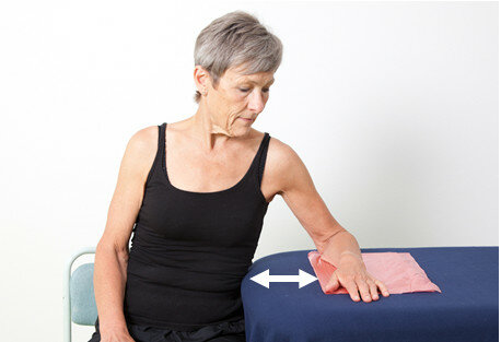 Øvelse 9 - Skub til siden: Sid med siden mod et bord. Læg underarm og hånd oven på klud eller pose. Sænk skulderen. Hold overkroppen i ro. Skub underarmen ud til siden, så afstanden til kroppen øges. Før armen tilbage igen.