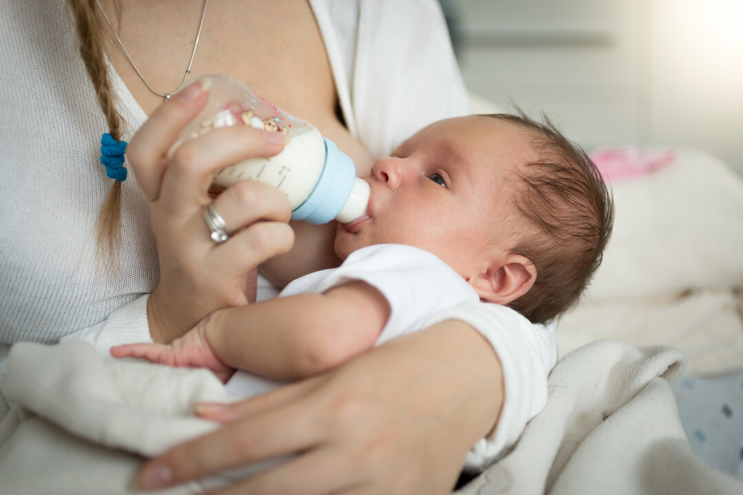 The picture shows a baby being feed with a bottle.