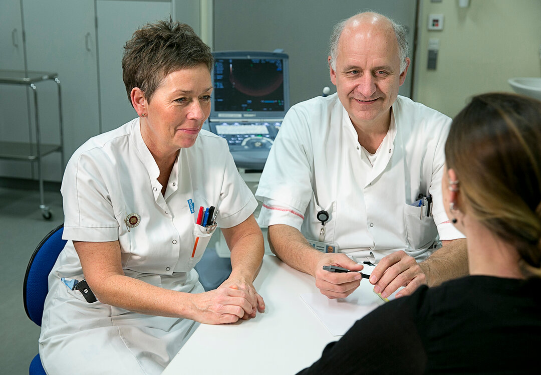 Billedet viser en sygeplejerske og en læge tale med en patient.