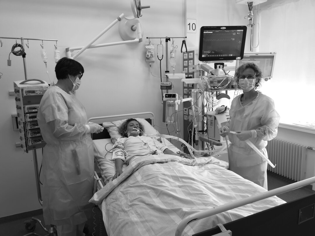 Patient ligger i seng, med en sygeplejerske på hver side af sengen. 