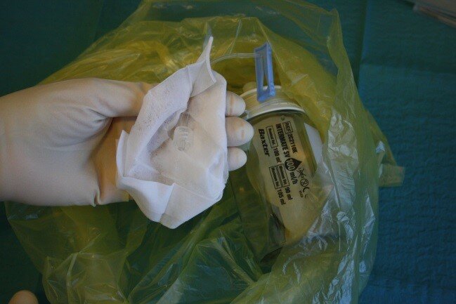 Billedet viser håndteringen af den tomme pumpe, der er kommet i en gul plastpose.